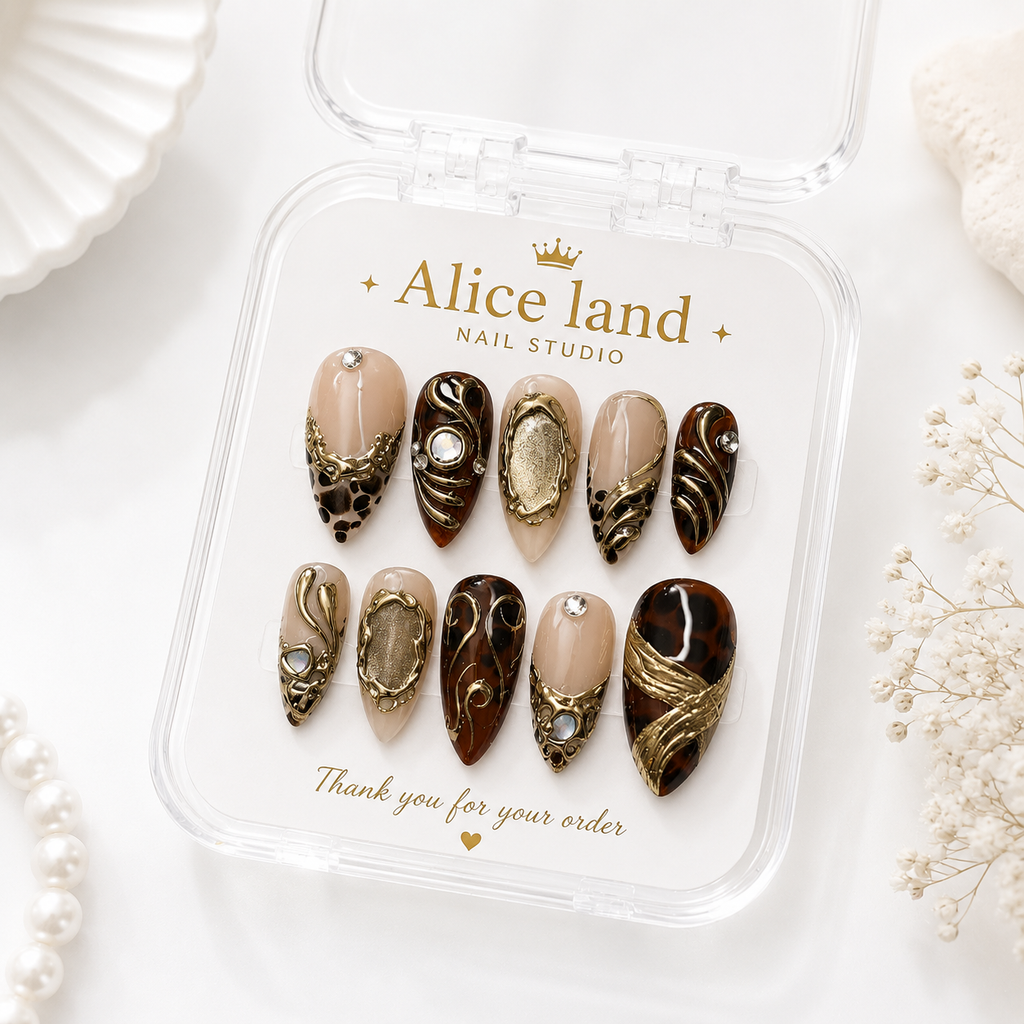 A set of 10 decorative press-on nails displayed in a clear plastic case labeled 'Alice land NAIL STUDIO'. The nails feature a mix of nude beige, dark brown, and metallic gold designs with rhinestone accents, set against a white background with decorative pearl and dried flower props.