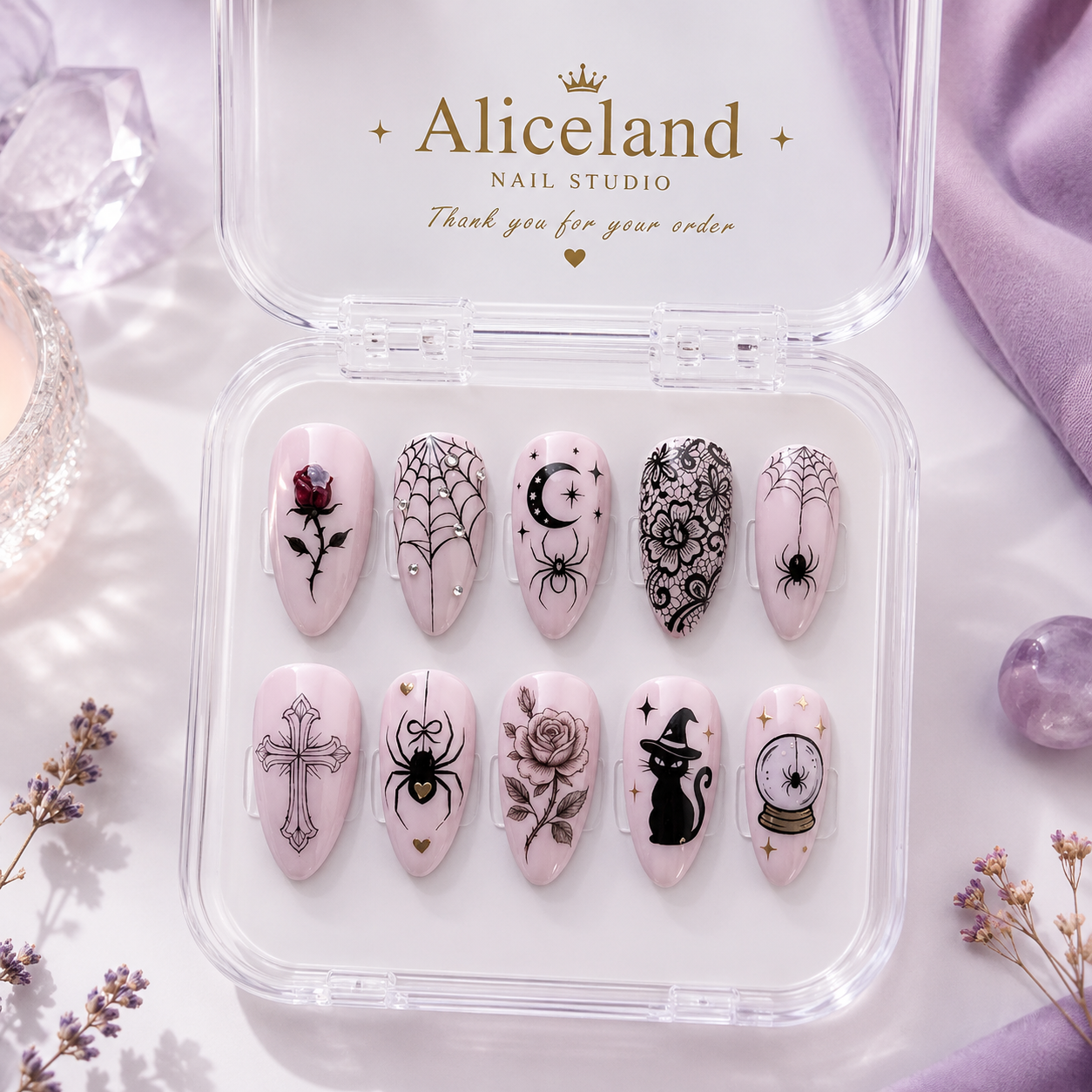 A set of ten decorative press-on nails displayed in a clear plastic case with the brand name 'Aliceland Nail Studio' printed on the inside lid. The nails have a pale pink base and feature various gothic and whimsical designs including spiders, a cat in a witch hat, a rose with a cross, a crescent moon, a spiderweb, and a crystal ball, accented with small gold glitter dots.